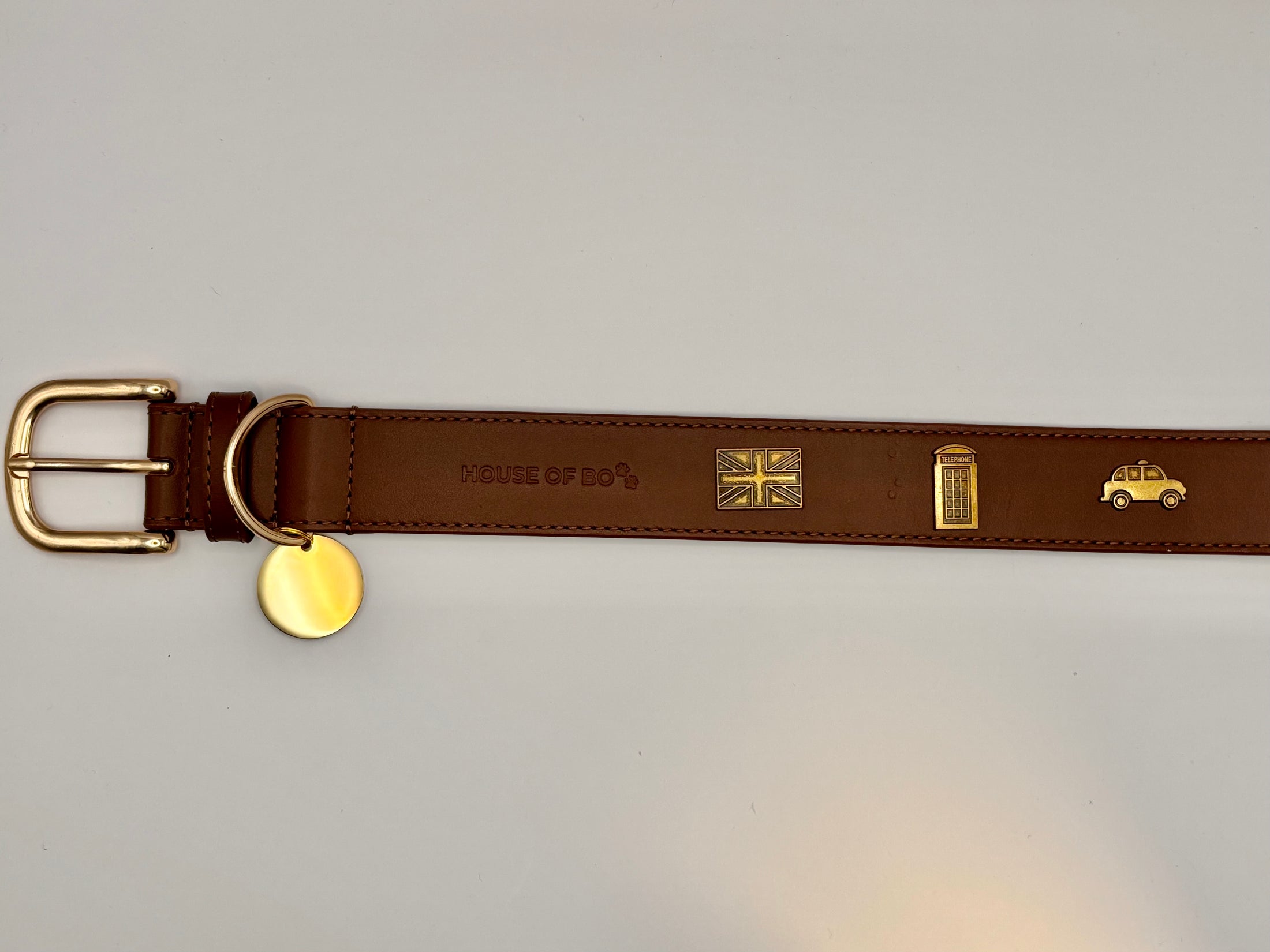 Brown leather belt with gold buckle and decorative elements on a light gray background