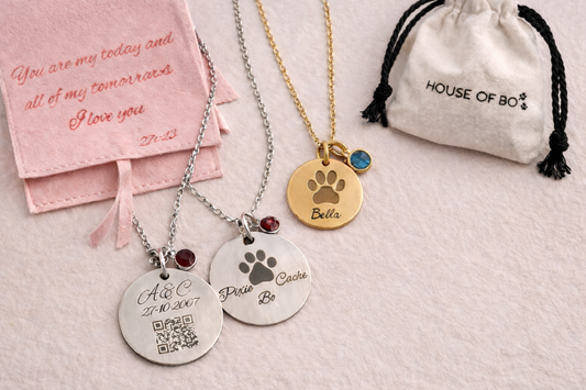 Three necklaces with paw print pendants and engraved text on a light pink background.