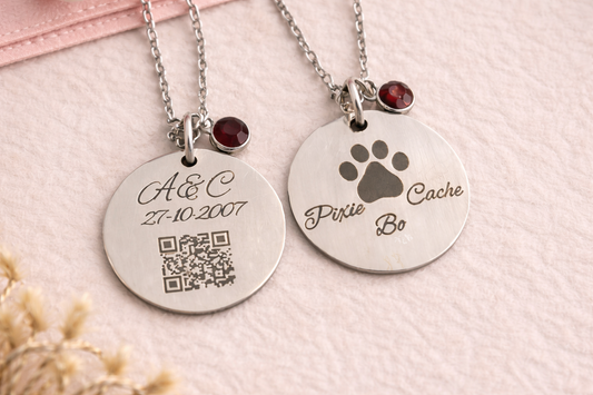 Two silver necklaces with engraved pendants on a light pink background